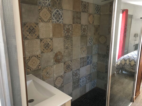 A bathroom with a tiled shower wall, a white sink, and a glass shower door.