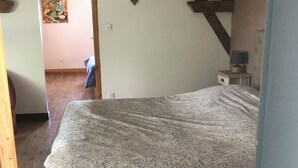 A bedroom with a bed, wooden beams, a small table with a lamp, and a wall decoration.