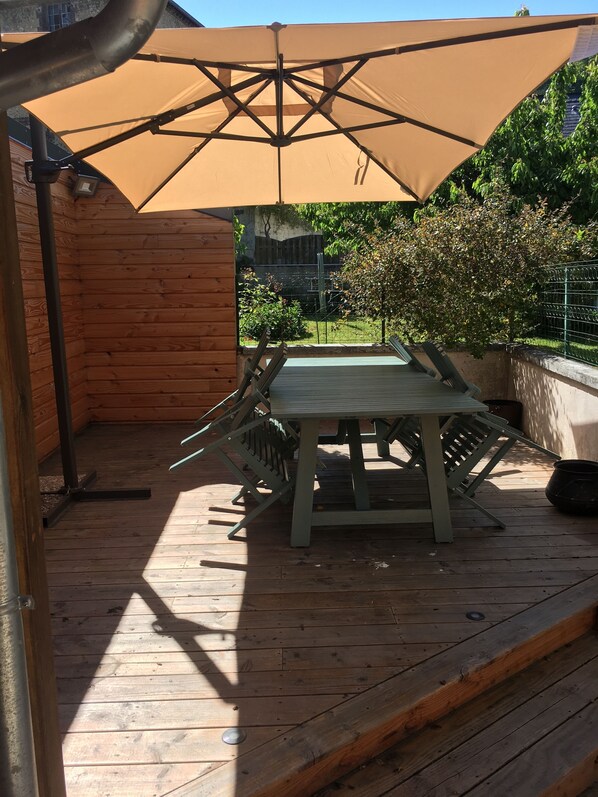 An outdoor wooden deck with a table and chairs, a large umbrella, and a metal fence in the background. - Charming town center house. A stone's throw from the old dock (Honfleur)