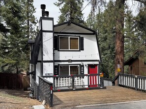 Un bâtiment à deux étages avec une porte rouge, une cheminée et une terrasse en bois.