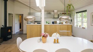 Eine moderne Küche mit einer zentralen Kochinsel, Pendelleuchten und einem Essbereich mit weißem Tisch und Stühlen.