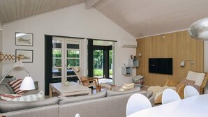 Ein modernes Wohnzimmer mit einer Couch, Sesseln, einem Esstisch und einem an der Wand befestigten Fernseher.
