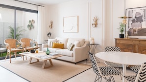 A modern living room with a sofa, coffee table, and chairs. There is a dining table with chairs, a potted plant, and a chandelier. - AJR Suite Loft - Holiday Apartment in Malaga (Málaga)