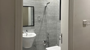 A modern bathroom with a large mirror, a sink, a toilet, and a shower.
