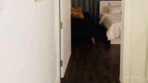 A narrow hallway leading to a bedroom with a bed, a bedside table, and a dark curtain.
