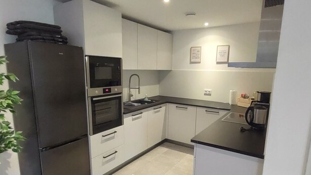A modern kitchen with white cabinets, a black refrigerator, a built-in oven, and a sink.