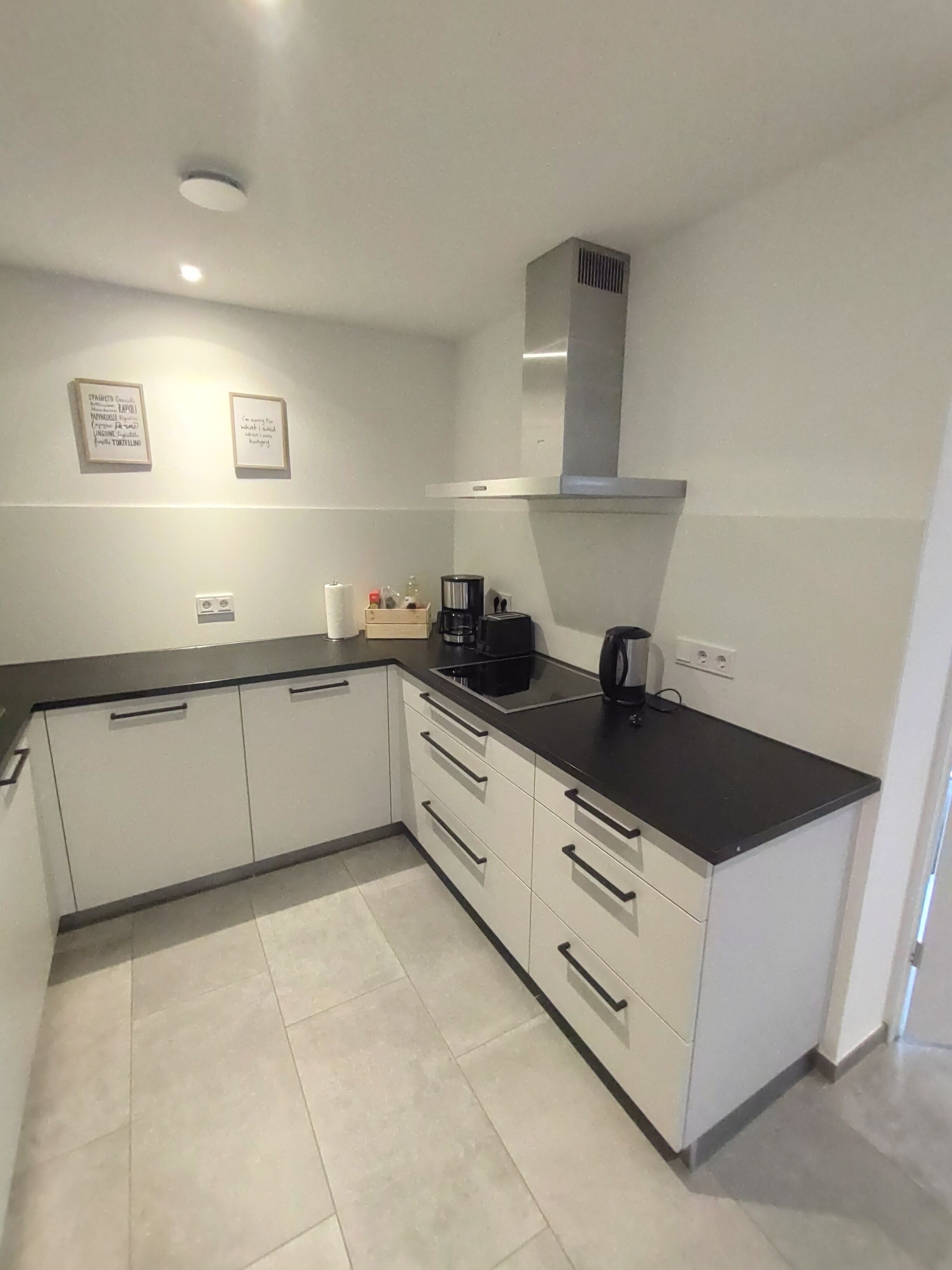 A modern kitchen with white cabinets, black countertops, and a black coffee maker.