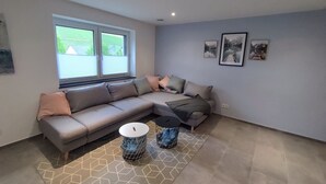 A modern living room with a sectional sofa, a patterned rug, and a window with blinds.