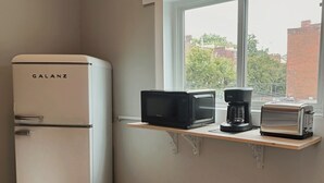 Pieni ja käytännöllinen keittiö, jossa on Galanz-merkkinen jääkaappi, mikroaaltouuni, leivänpaahdin ja kahvinkeitin, ja ne on sijoitettu hyllylle ikkunan viereen.