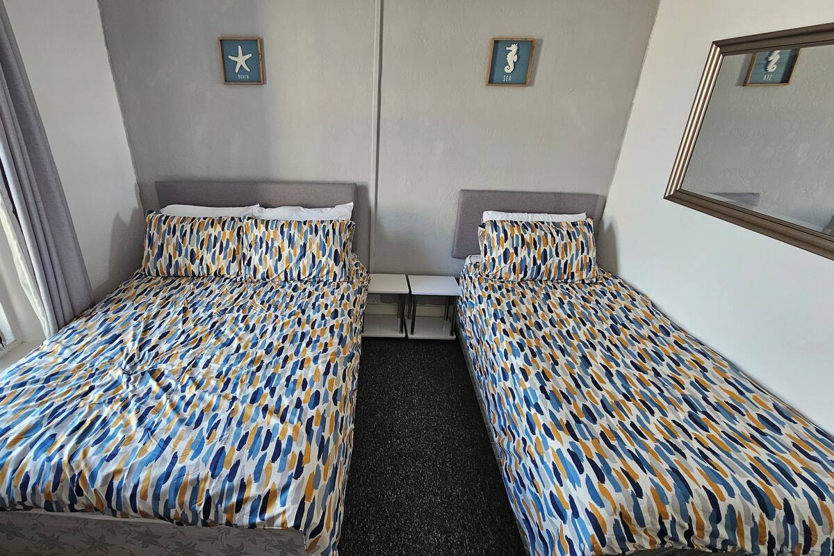 Habitación de hotel con dos camas, cada una con colcha estampada, una mesita de noche, un espejo y un cuadro con una estrella de mar y un caballito de mar.