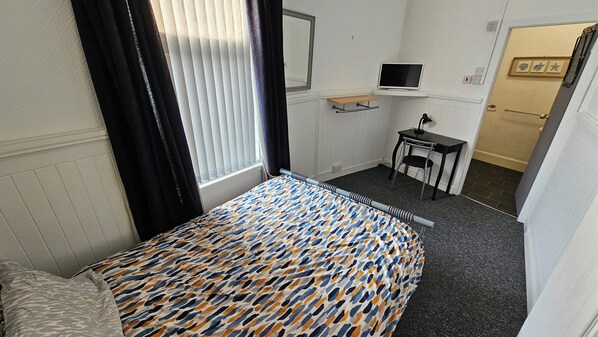 A small hotel room with a bed, a desk, a chair, a TV, and a door.