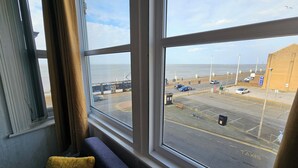 Ein Zimmer mit großem Fenster, Blick auf einen Parkplatz und einen Strand.