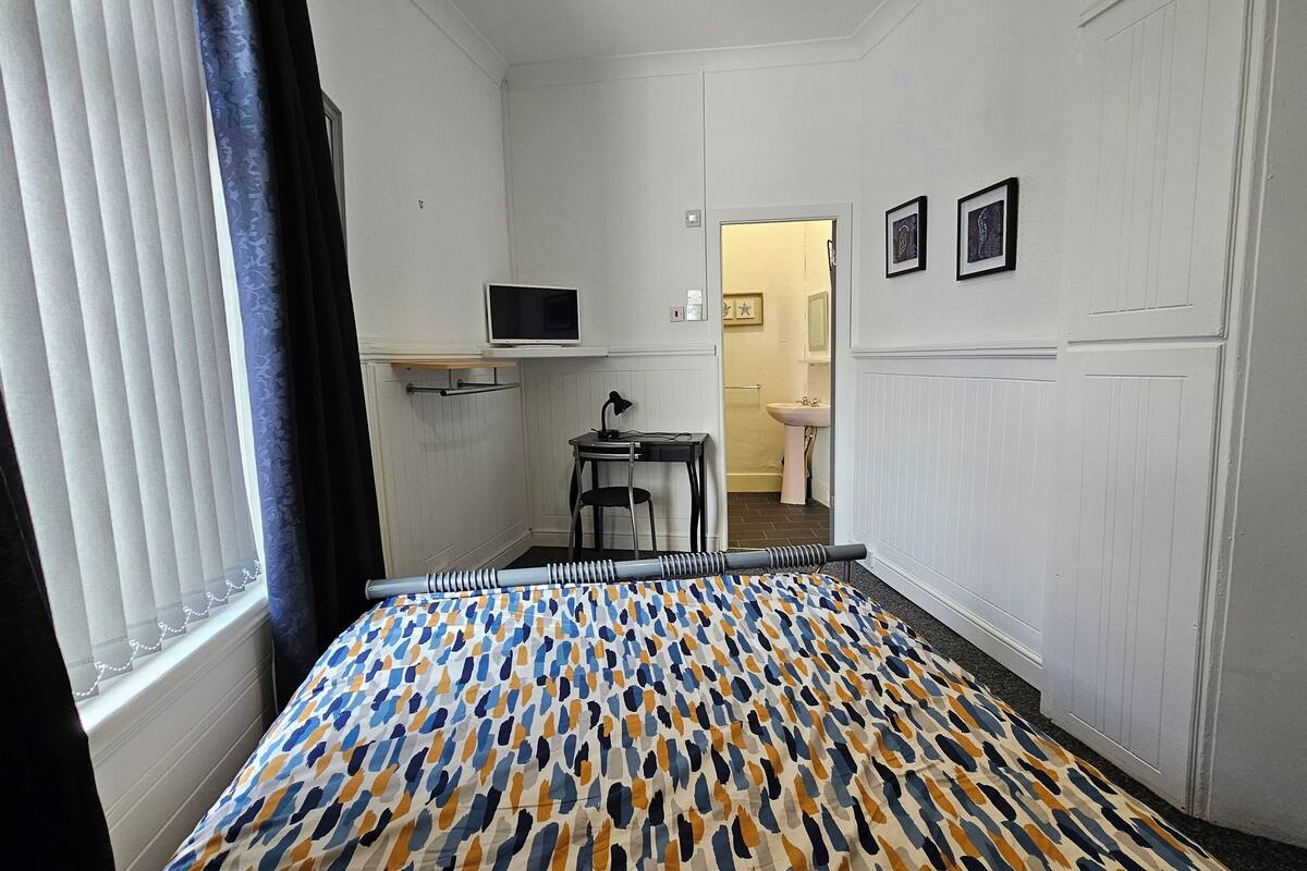 Habitación de hotel con cama, escritorio, silla, televisor y baño visible a través de una puerta abierta.