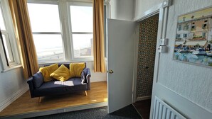 Ein Zimmer mit einer Couch, einer Tür, einem Fenster mit Vorhängen und einer Wand mit Muster.