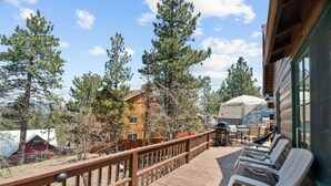Une terrasse en bois avec des chaises longues, un espace barbecue et une vue sur les chalets et les arbres environnants.