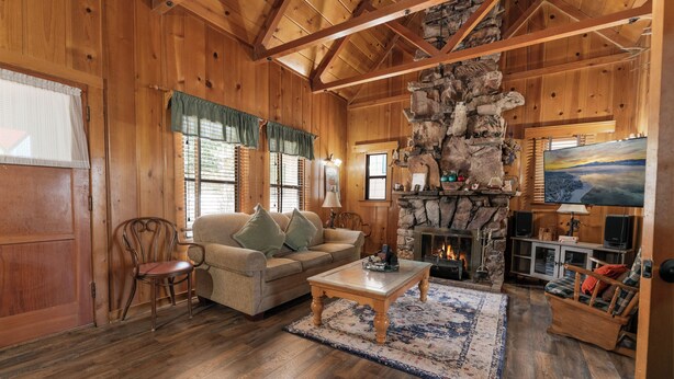 L’intérieur d’un chalet confortable, avec une cheminée en pierre, des meubles en bois et un téléviseur.