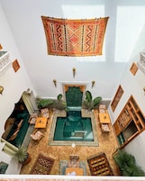 Um quarto amplo com piscina verde central, um tapete pendurado com padrão e diversas opções de assento.