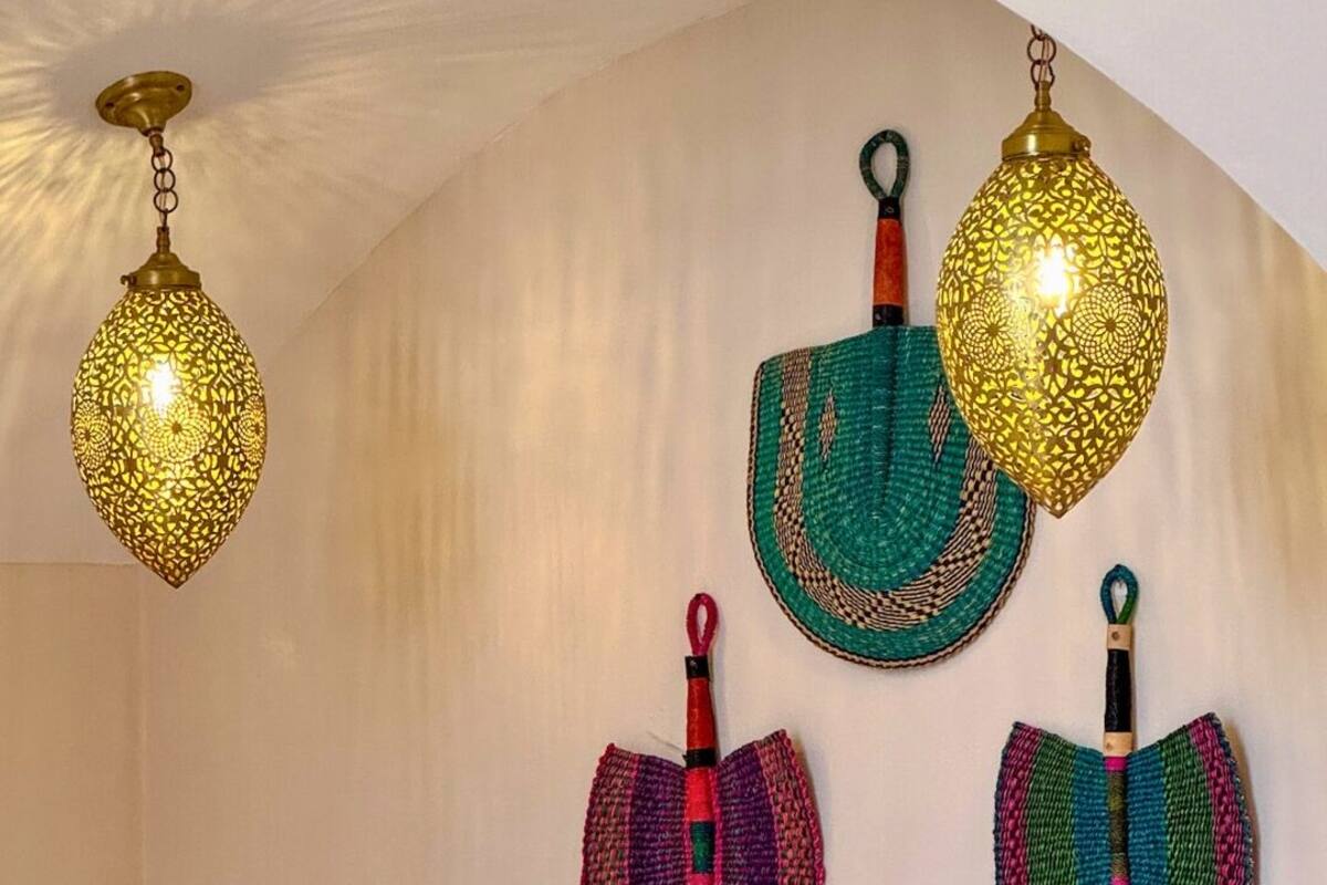 A room with a white curved ceiling, a bed with white linens, and four hanging lamps with intricate designs.