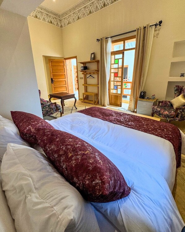 A hotel room with a large bed, a wooden desk, a chair, and a wardrobe.