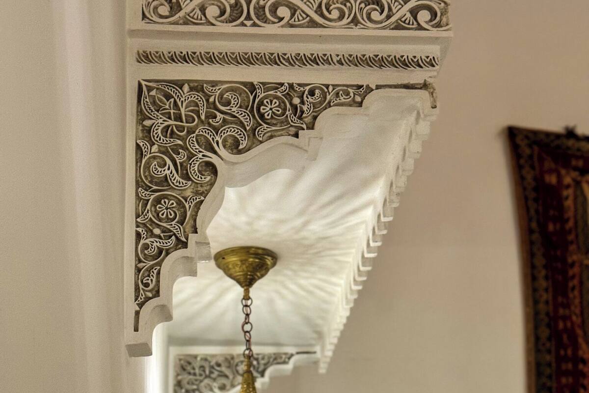 A hanging ornate lamp with intricate patterns, a decorative wall with carved designs, and a patterned textile hanging on the wall.