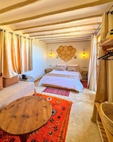 Um quarto aconchegante com uma cama, duas mesas de cabeceira, uma mesa de centro de madeira e um tapete vermelho estampado.