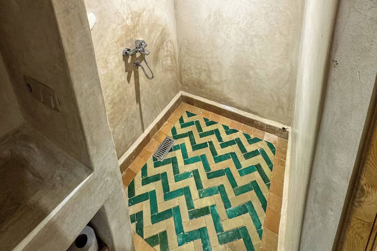 A small, enclosed shower area with a chevron-patterned floor, a handheld showerhead, and a wall-mounted faucet.