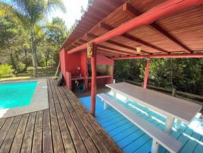 Une terrasse en bois avec une piscine, un espace barbecue et une table de pique-nique.