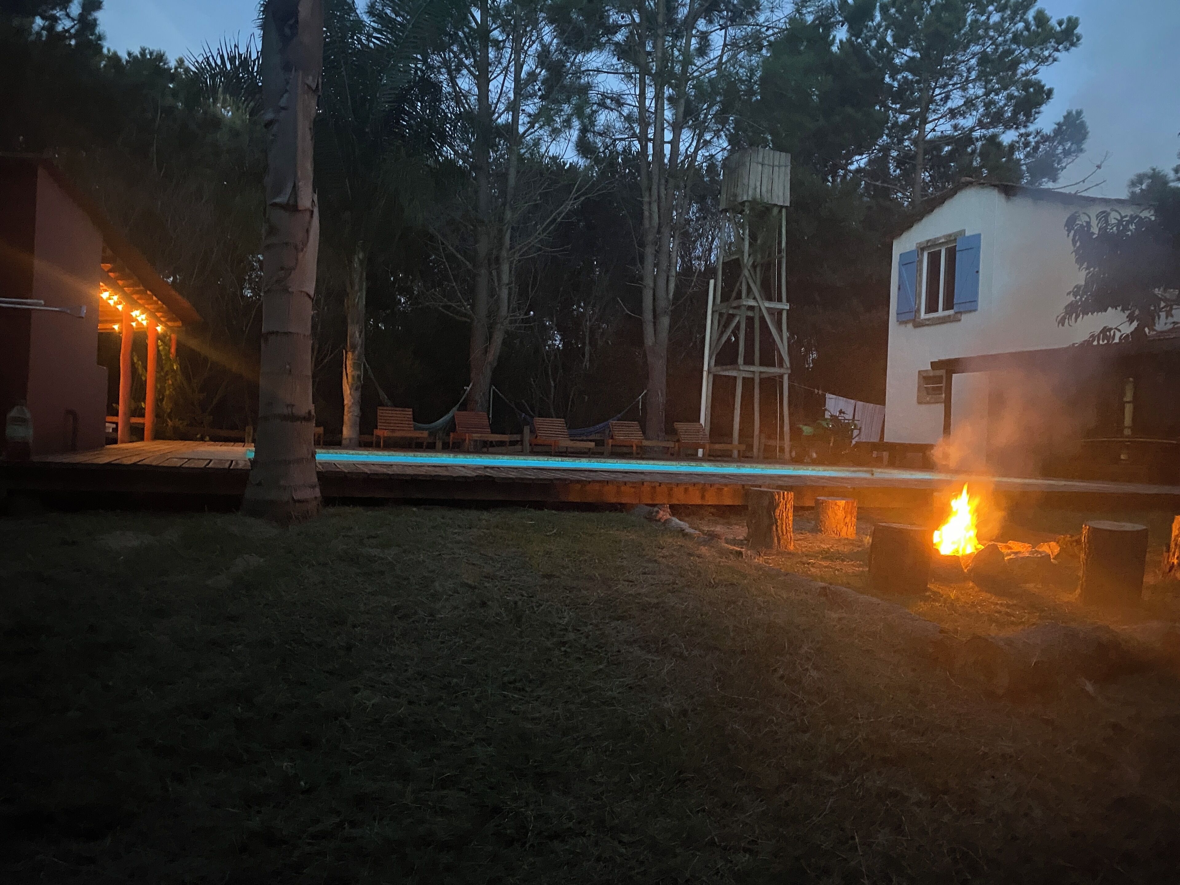 Ein Poolbereich mit Holzliegen, einer Hängematte und einer Feuerstelle.