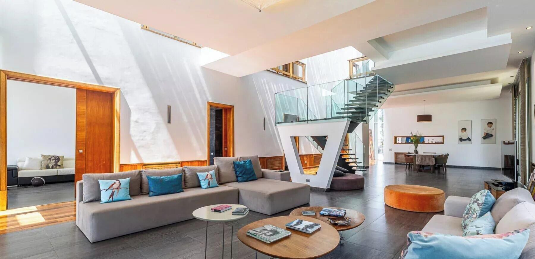 A spacious living area with a modern staircase, a sofa set, and a dining area.