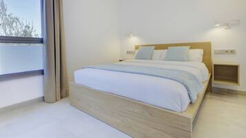 Un dormitorio moderno con estructura de cama de madera, ropa de cama blanca y vista a árboles a través de una ventana.