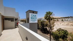 Un edificio con un letrero que dice "CALM BEACH APARTMENTS" y vista a una playa y edificios al fondo.