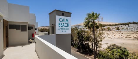 A building with a sign reading "CALM BEACH APARTMENTS" and a view of a beach and buildings in the background.