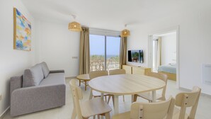 Una sala de estar moderna con un sofá gris, una mesa de comedor redonda de madera y un televisor montado en la pared.