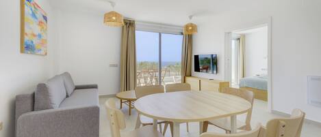A modern living room with a grey sofa, a round wooden dining table, and a TV mounted on the wall.