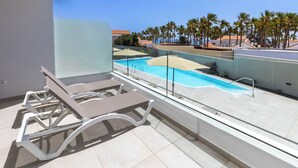 Un área de piscina en la azotea con sillones de descanso y vista despejada a palmeras y edificios al fondo.