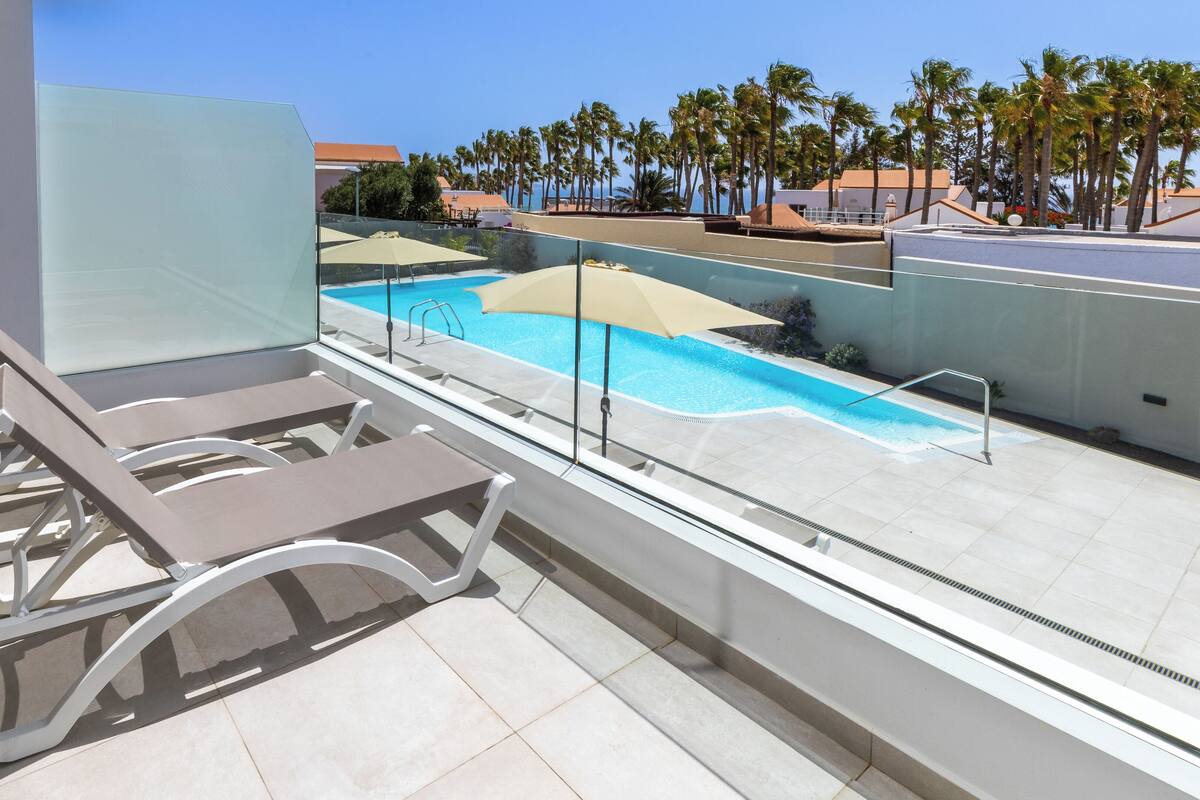 A rooftop pool area with lounge chairs and a clear view of palm trees and buildings in the background.