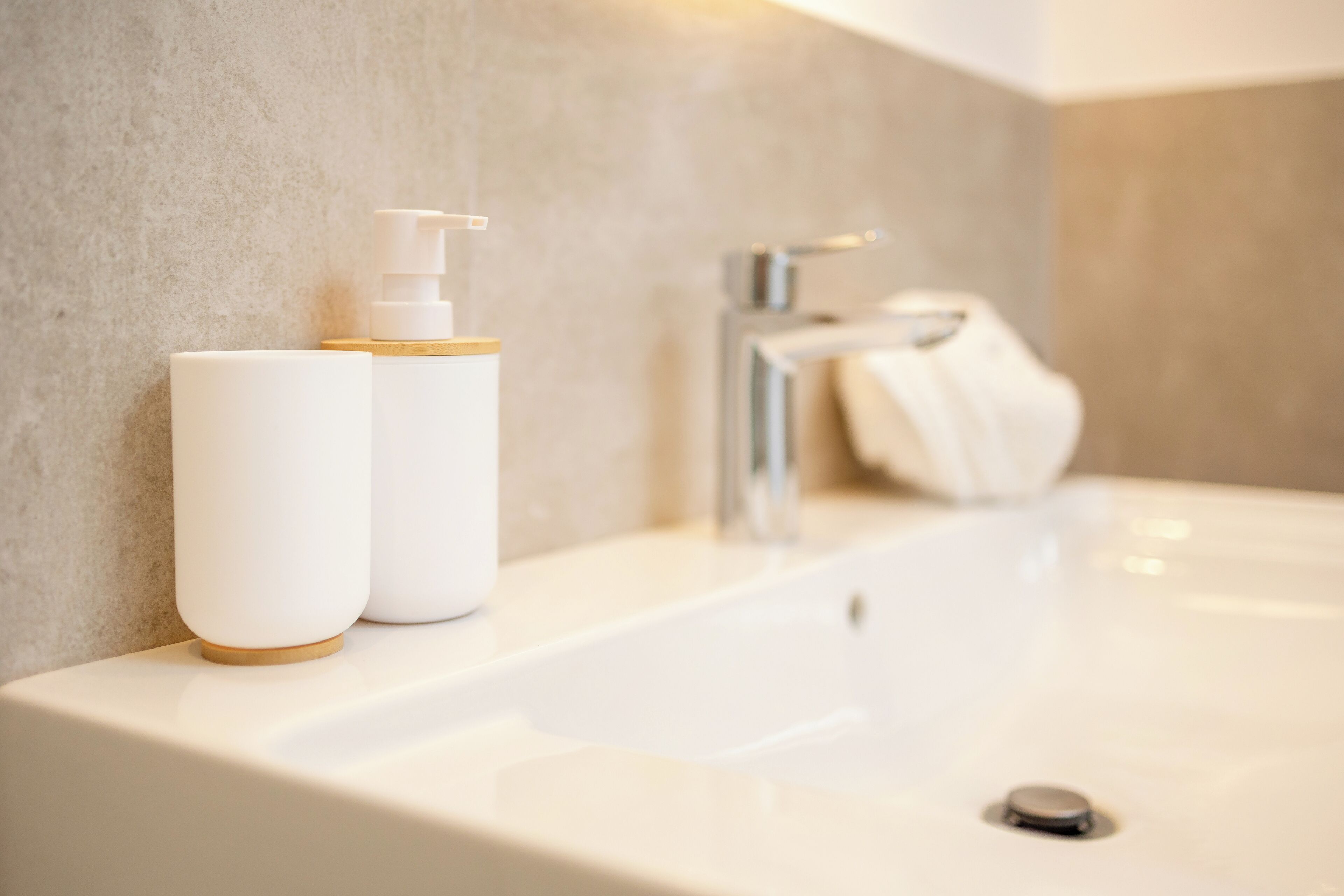 A bathroom with a white sink, a towel, and two white bottles with pumps.