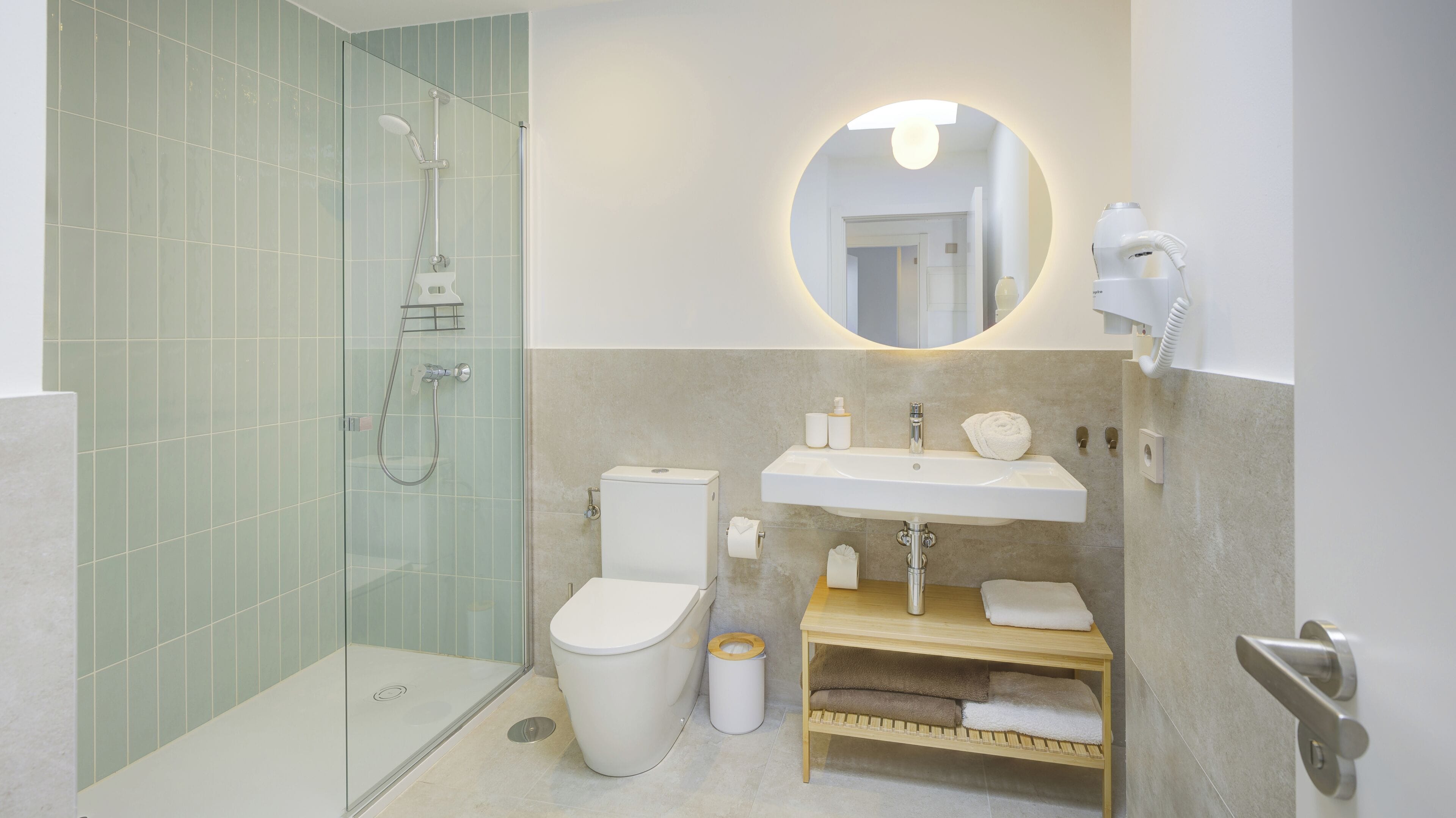 A modern bathroom with a glass shower enclosure, a toilet, a sink with a mirror above it, and a towel rack.