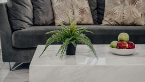 Een moderne woonkamer met een grijze bank, een witte salontafel en een pot met een varen.