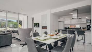 A modern dining area with a white table set for four, surrounded by grey chairs.