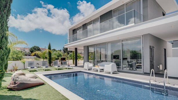 Een modern zwembadgedeelte met een helderblauw zwembad, witte ligbedden en een glazen patio.