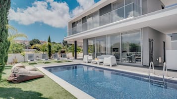 A modern pool area with a clear blue pool, white lounge chairs, and a glass-enclosed patio.