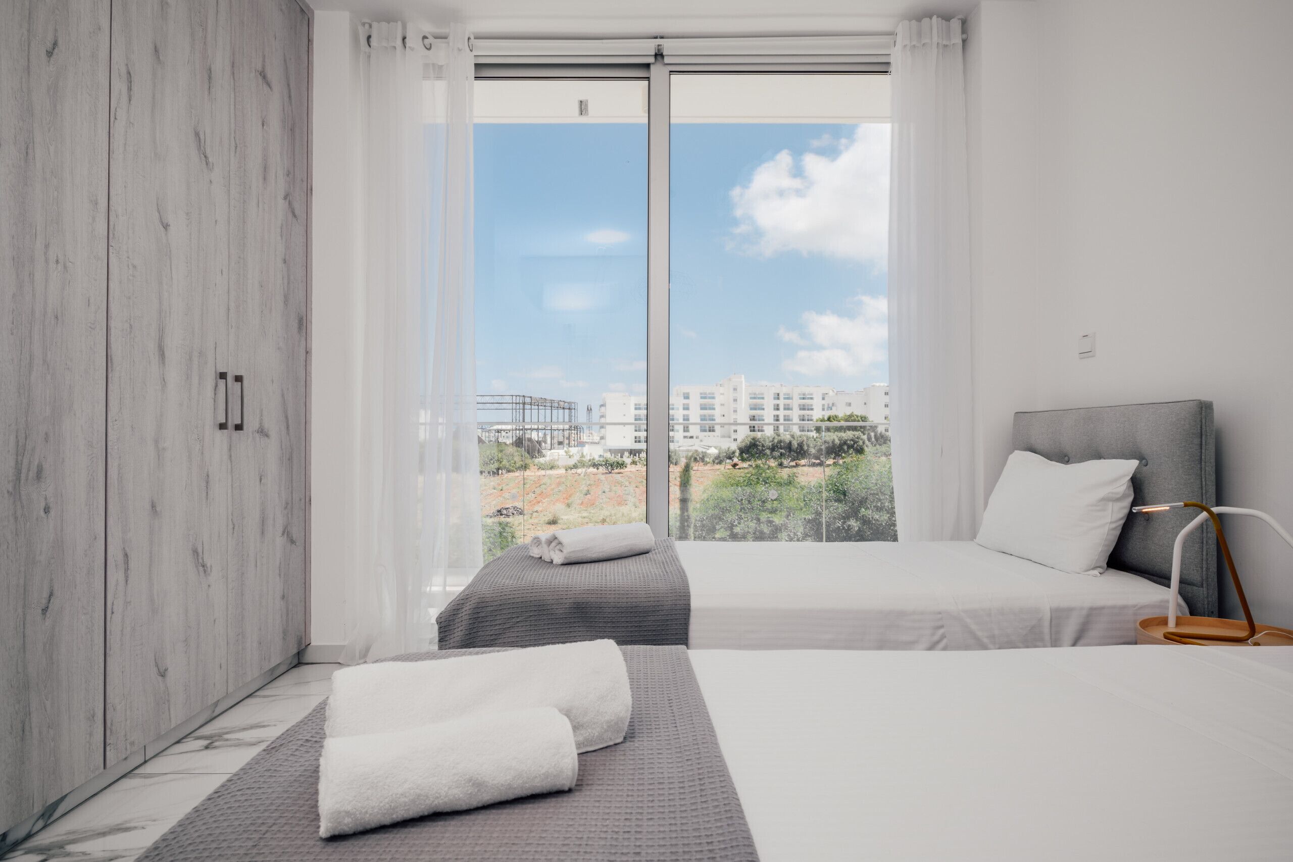 Een moderne hotelkamer met twee bedden, een groot raam met uitzicht over de stad en een houten kast.