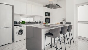 Een moderne keuken met een centraal eiland, barstoelen, een wasmachine en een inbouwoven.
