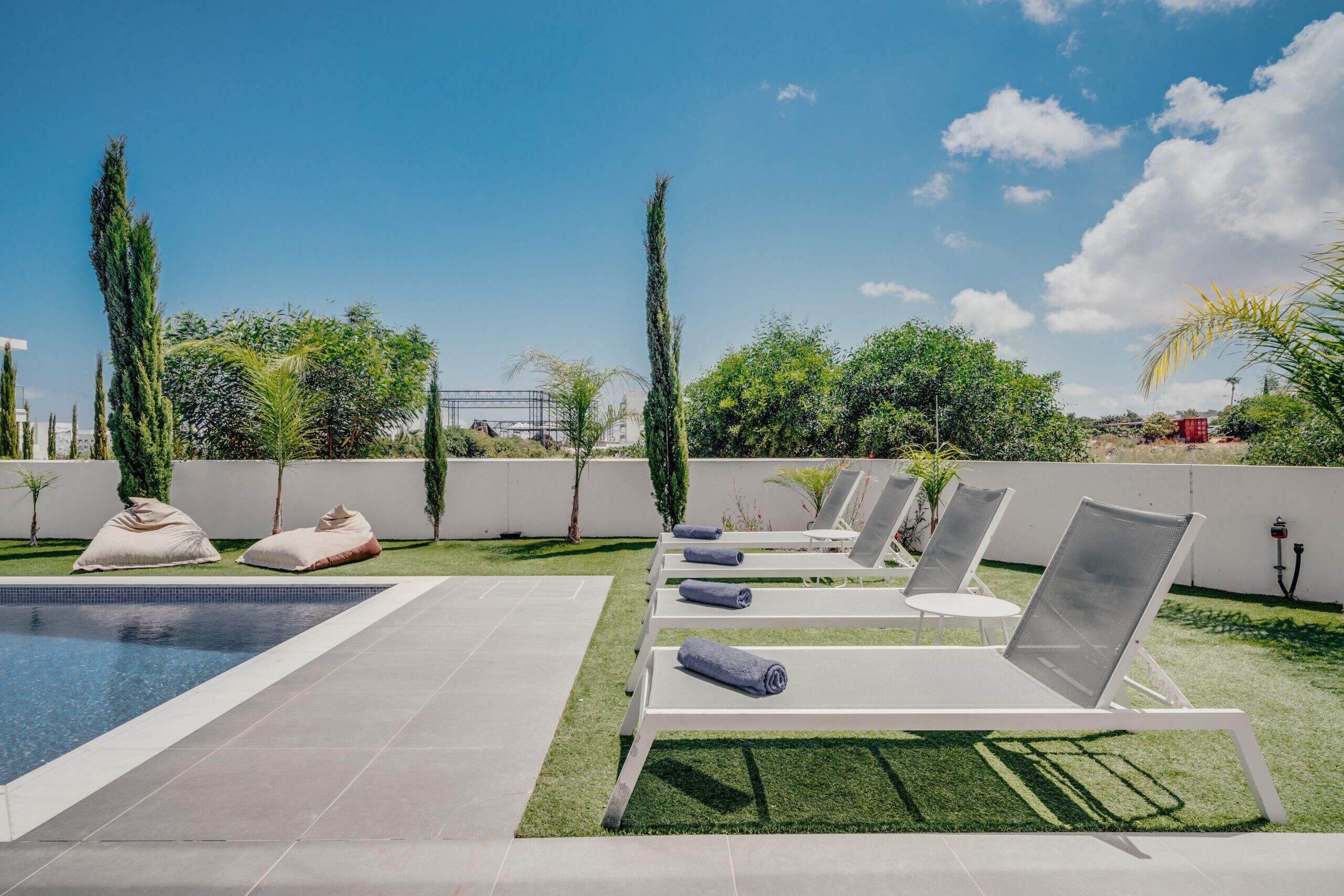 Un espace piscine aménagé sur le toit, avec des chaises longues, une piscine et une végétation luxuriante tout autour.