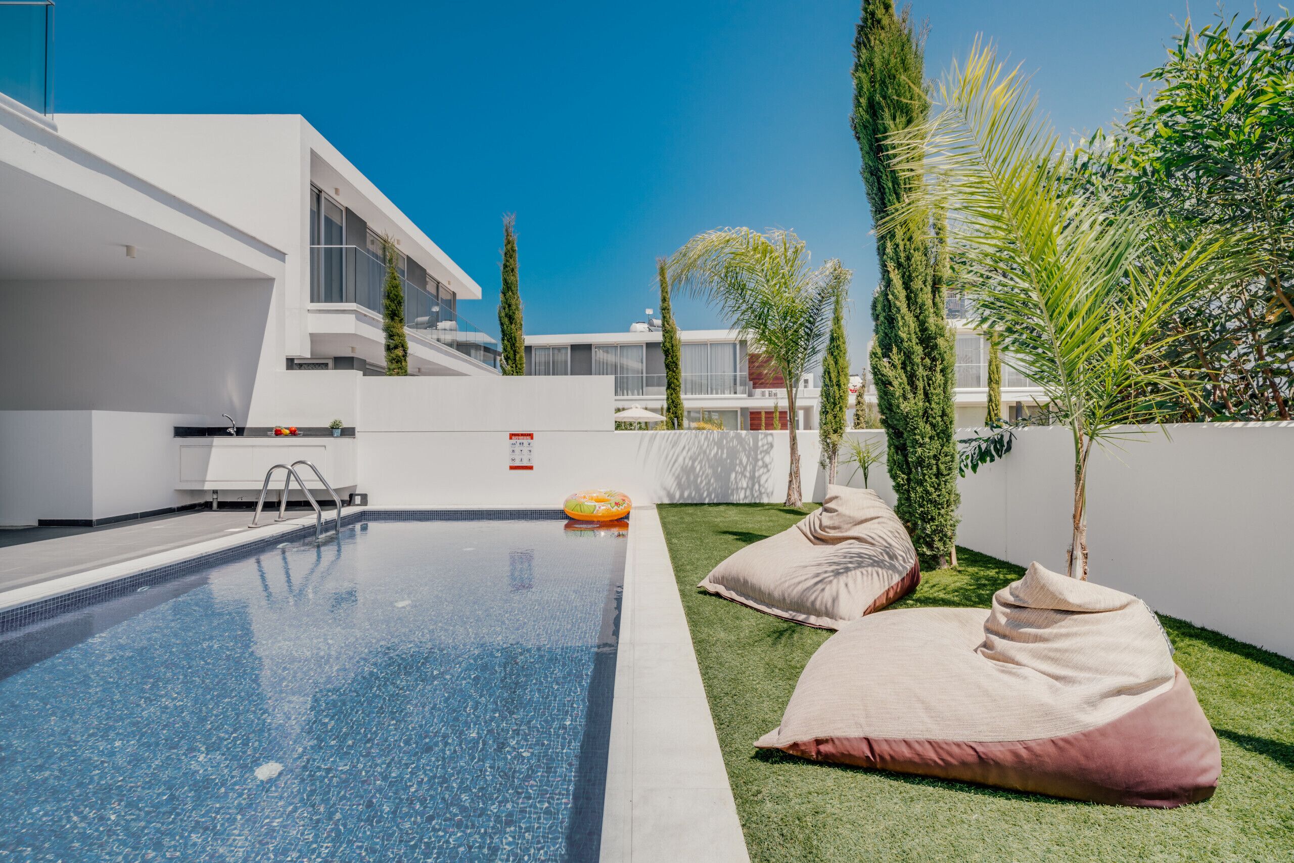 A modern outdoor pool area with a clear blue pool, a lounge chair, and a small inflatable float.
