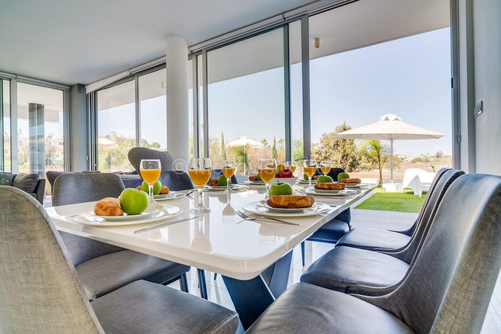 A dining area with a table set for breakfast, large windows, and a view of the outdoors.