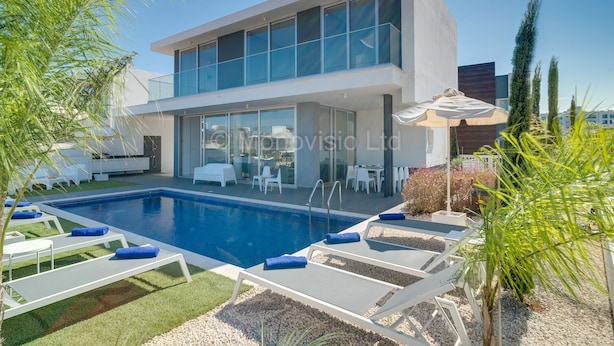 Une maison moderne à deux étages dotée d’une piscine, d’un espace salon extérieur et d’un patio couvert.