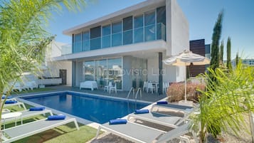 Uma casa moderna de dois andares com piscina, área de estar externa e varanda coberta.