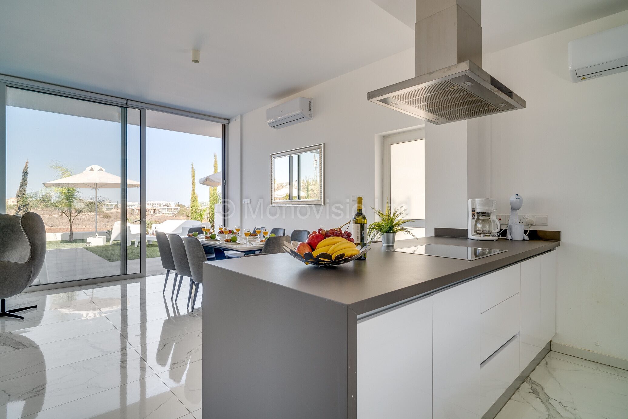 A modern kitchen with a large island, a dining area with chairs, and a view of the outdoors.